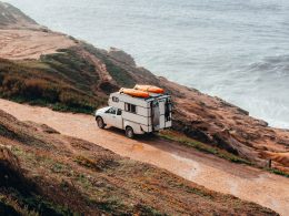 Truck camper with surboards mounted to the roof driing along the coast of the ocean.
