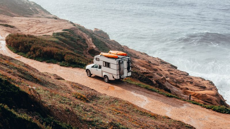 Truck camper with surboards mounted to the roof driing along the coast of the ocean.