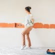 Woman dancing with her earbuds in while painting a wall.
