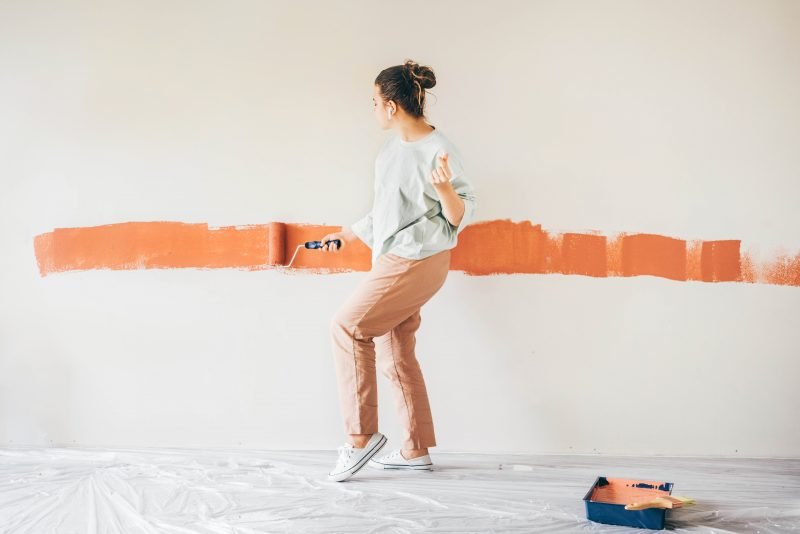 Woman dancing with her earbuds in while painting a wall.