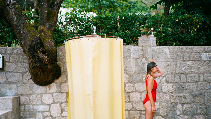 A woman shower outside a campground station in her red bathing suit.