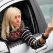 Angry woman aggressively gives the middle finer out her car window as she drives.