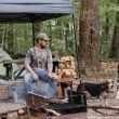 A man and his dogs at his campsite setup in the woods.