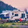 A hybrid camper parked in a campground near forested mountains at dusk.
