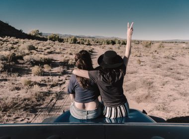 Two woman sit on the hood of their vehicle in the desert on a boondocking trip
