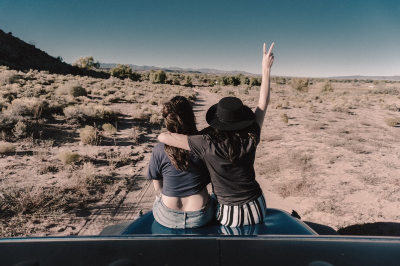 Two woman sit on the hood of their vehicle in the desert on a boondocking trip