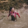 A woman smiling and laughing as she stands in a mud pit up to her butt.