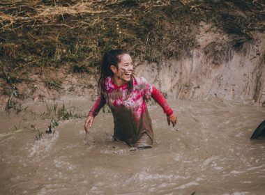 A woman smiling and laughing as she stands in a mud pit up to her butt.