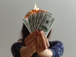 Woman holds several one hundred dollars bills that are lit on fire, the literal idea of wasting money.