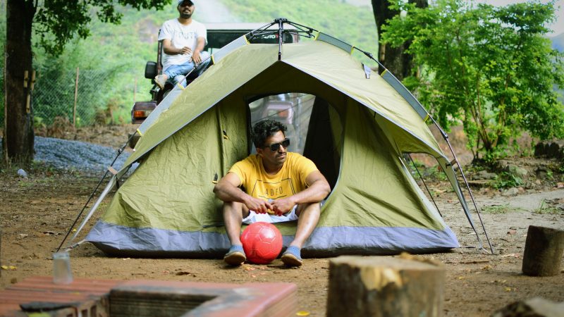 Man hanging out of his tent with his soccer ball while camping in the woods.