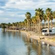 RVs parked at a campground along a beautiful river front on a warm sunny day.