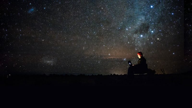 Sitting outside on a laptop using the internet underneath starts and satellites in the night sky