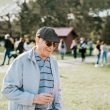 Senior man smiles as he walks outside with wine at an outdoor event.
