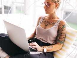 Young, beautiful, tattooed woman sits corss-legged with her laptop