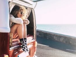 A woman in shorts and cute socks sitting with her legs out the back of her camper van enjoying van life.