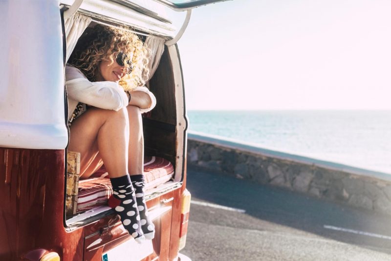 A woman in shorts and cute socks sitting with her legs out the back of her camper van enjoying van life.