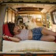 A woman living van life, lounging in the bed of her campervan with her dog