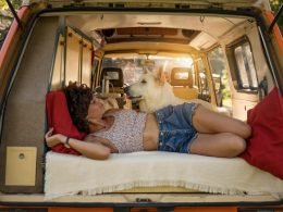 A woman living van life, lounging in the bed of her campervan with her dog