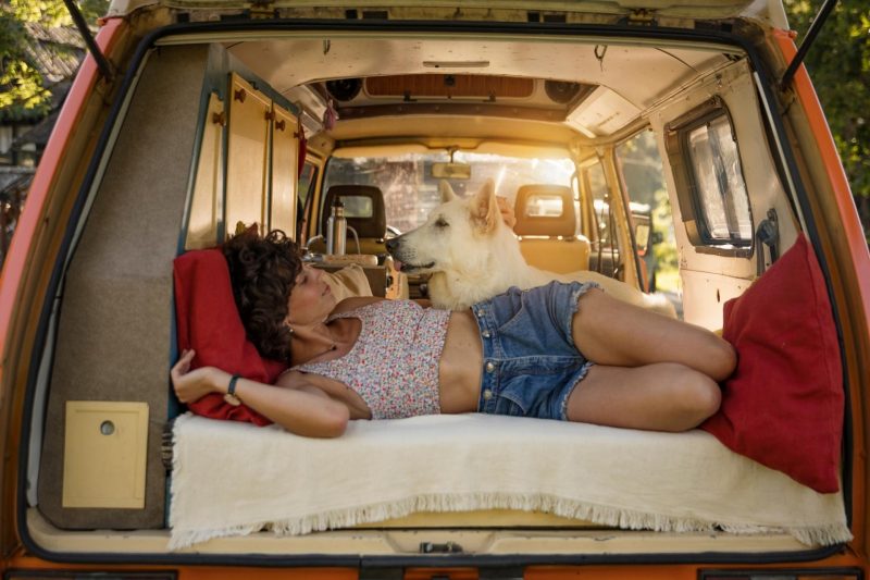 A woman living van life, lounging in the bed of her campervan with her dog