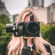 A video camera hides the face of the blonde woman shooting the video.