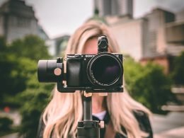 A video camera hides the face of the blonde woman shooting the video.