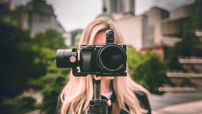 A video camera hides the face of the blonde woman shooting the video.