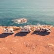 Two motorhomes and a camper van are parked along a cliff next to the the ocean coast