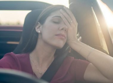 A tired driver leans her head in her hand as she embarks on a long road trip