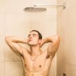 A shirtless man showers in a tile shower with a rain head.