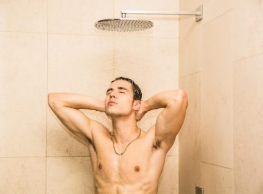 A shirtless man showers in a tile shower with a rain head.
