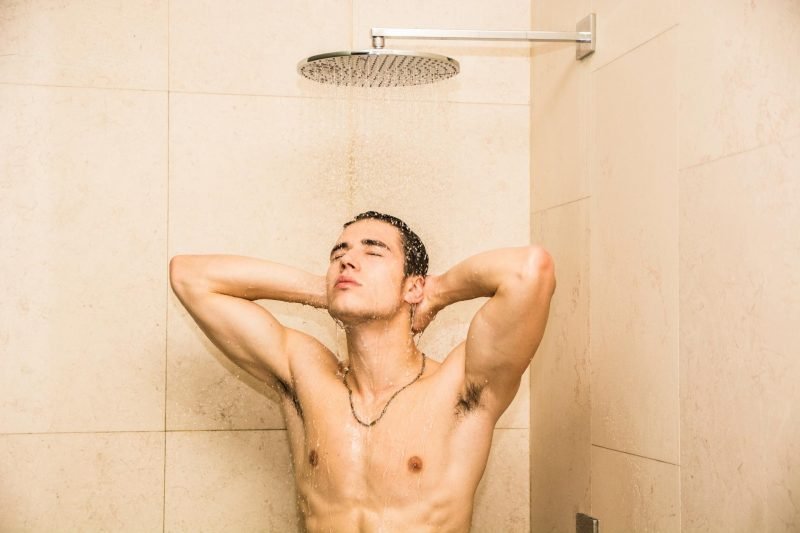 A shirtless man showers in a tile shower with a rain head.