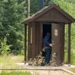 A person entering an outdoor restroom with a vault toilet at a park.