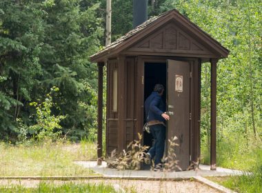 A person entering an outdoor restroom with a vault toilet at a park.