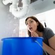 Woman shocked at the water leaking from the pipes below her sink.