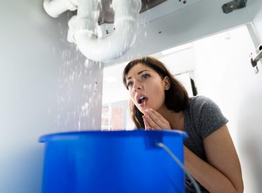 Woman shocked at the water leaking from the pipes below her sink.