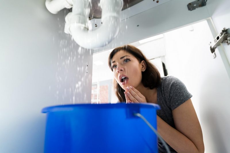 Woman shocked at the water leaking from the pipes below her sink.