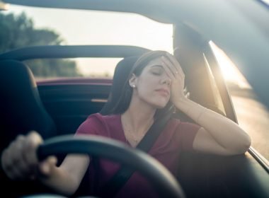A tired driver leans her head in her hand as she embarks on a long road trip