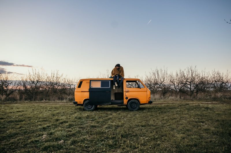 A couple cuddles in a blanket on top of their campervan