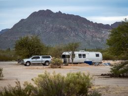 A Airstream travel trailer and truck parked in the dessert with solar panels.