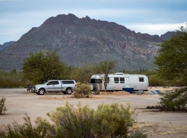 A Airstream travel trailer and truck parked in the dessert with solar panels.
