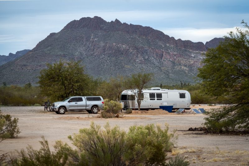 A Airstream travel trailer and truck parked in the dessert with solar panels.