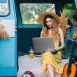 A beautiful woman with long hair and a dress works on her computer from her camper van and lives the van life on the road.