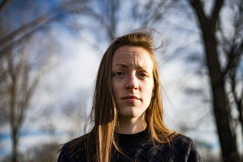 A worn out women looks empty at the camera as she stands outside in the lowlight of winter.