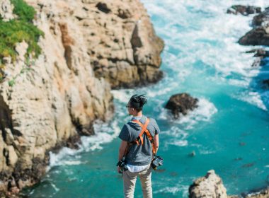 A man overlooks the waves crashing below him along the rocky coastline in Big Sur.