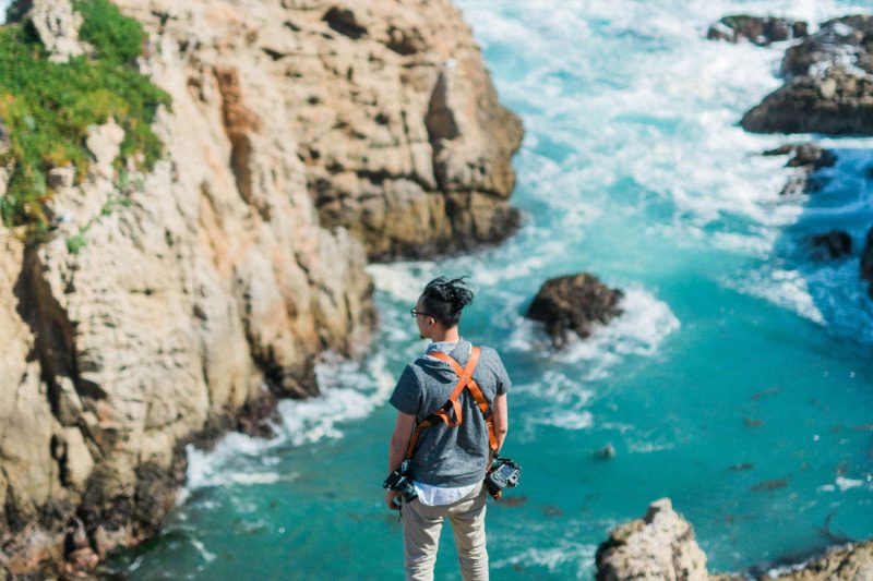 A man overlooks the waves crashing below him along the rocky coastline in Big Sur.