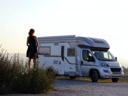 Silhouette of a woman standing outside of a class c motorhome as the sun sets over a field.
