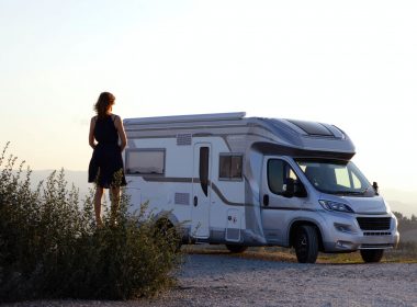 Silhouette of a woman standing outside of a class c motorhome as the sun sets over a field.