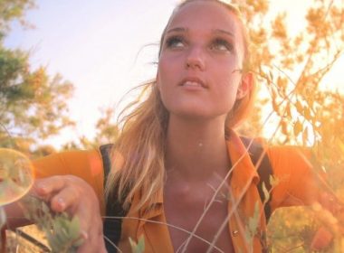 A woman crouches in the bushes in the woods.