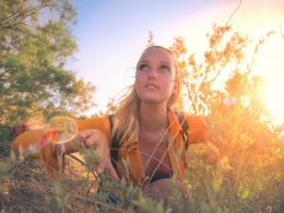 A woman crouches in the bushes in the woods.