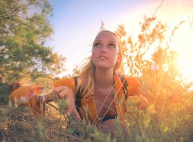 A woman crouches in the bushes in the woods.